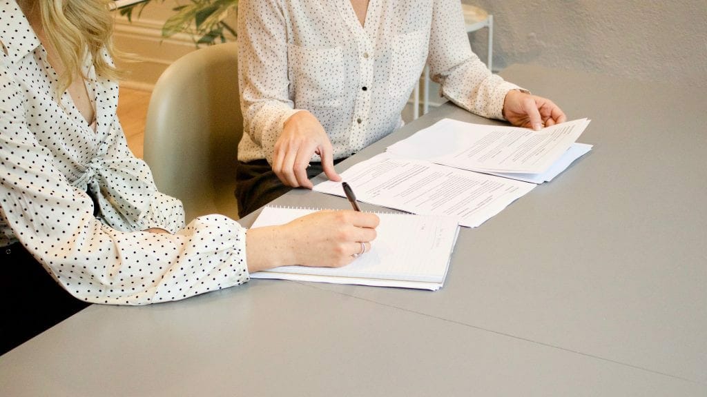 two people sitting at a table discussing forms in front of them on table