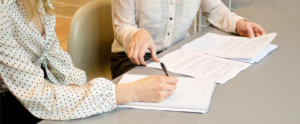 two people sitting at a table together writing on documents